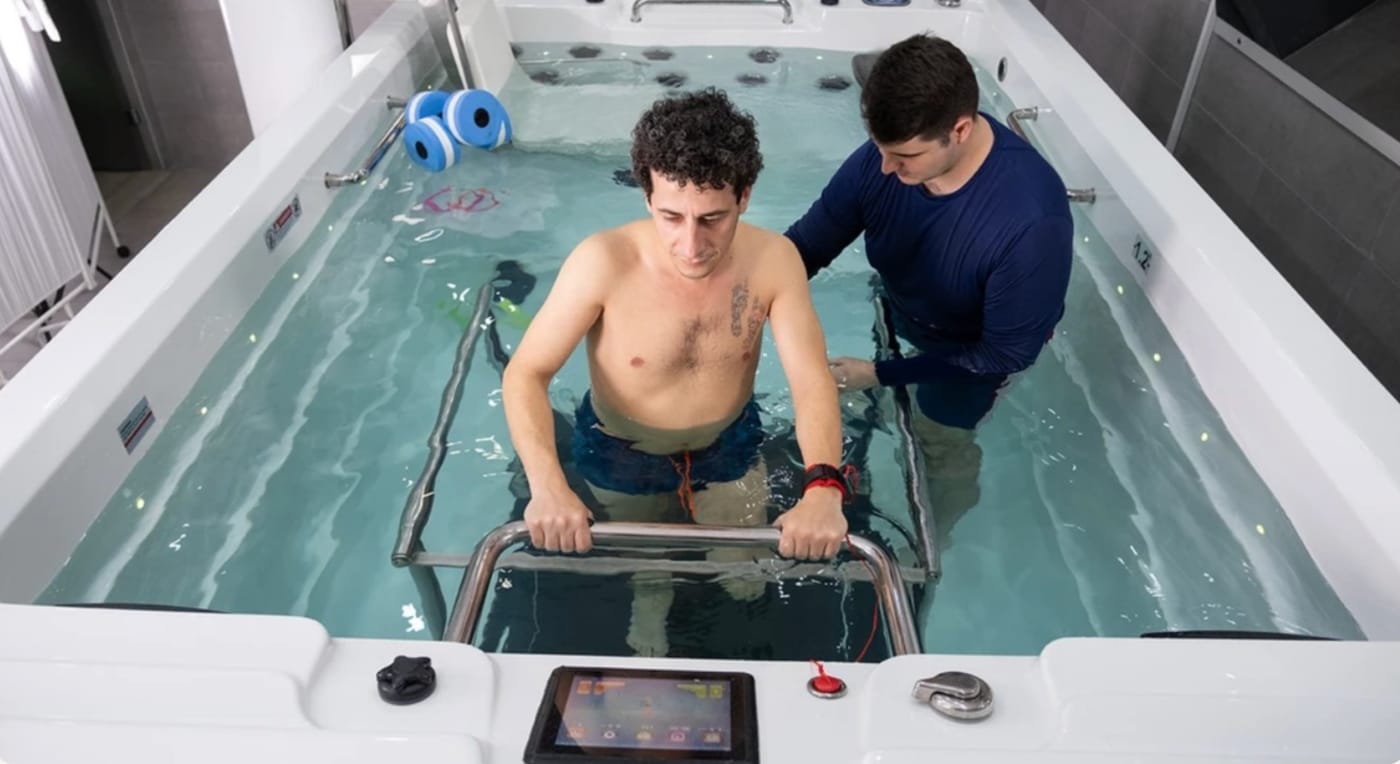 A patient walking in a heated hydrotherapy pool with a therapist in the water